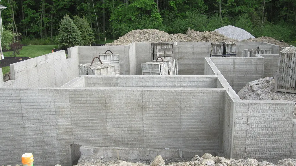Poured concrete foundation walls of a house, with soil and gravel piles waiting for backfill.