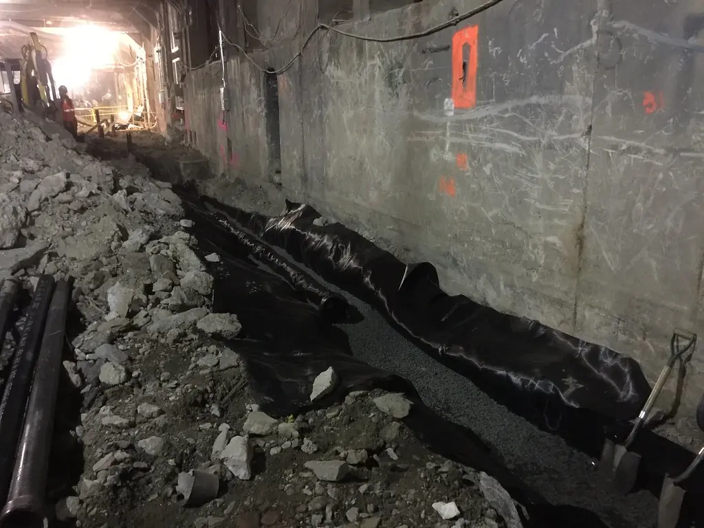 Perforated drainage pipe and a black membrane laid in gravel beside a concrete wall.