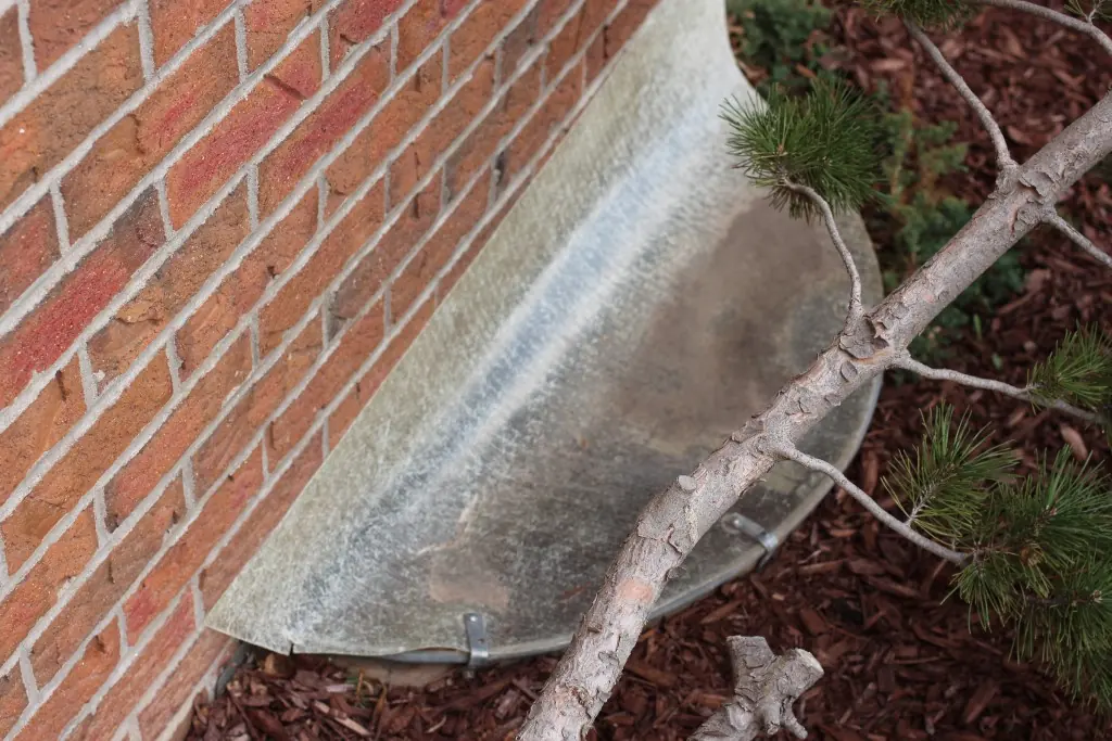Plastic cover over a basement window well beside a brick foundation wall.